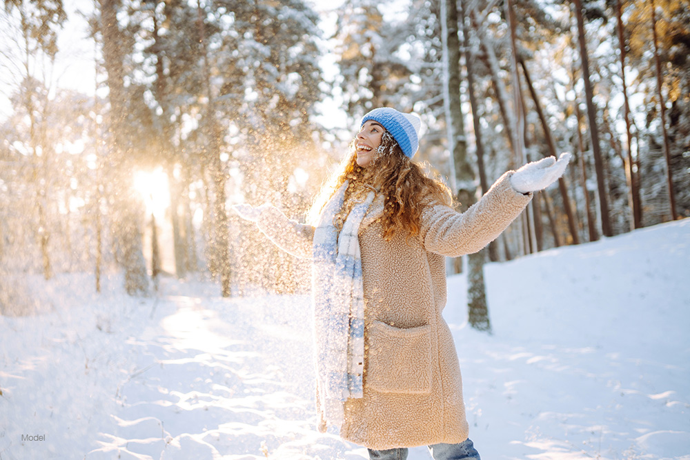 woman in winter wear, playing with snow in a forest.